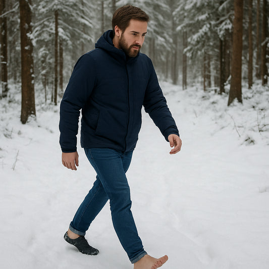 A man walking barefoot in a snowy forest, wearing TJÅKKO barefoot shoes. Alt: barfotaskor herr naturlig rörelse i vinterlandskap.