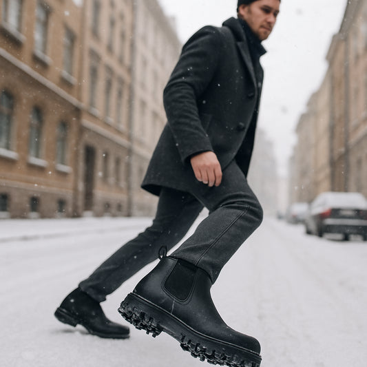 En man i stilrena chelsea boots herr vinter som går längs en snötäckt stadsgata, med fokus på den robusta sulan och det vattenavvisande lädret. Alt: chelsea boots herr vinter för stadspromenader – varm, vattentät och med bra grepp