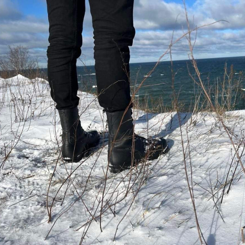 M77 militärkängor på en snöig slänt med havsutsikt